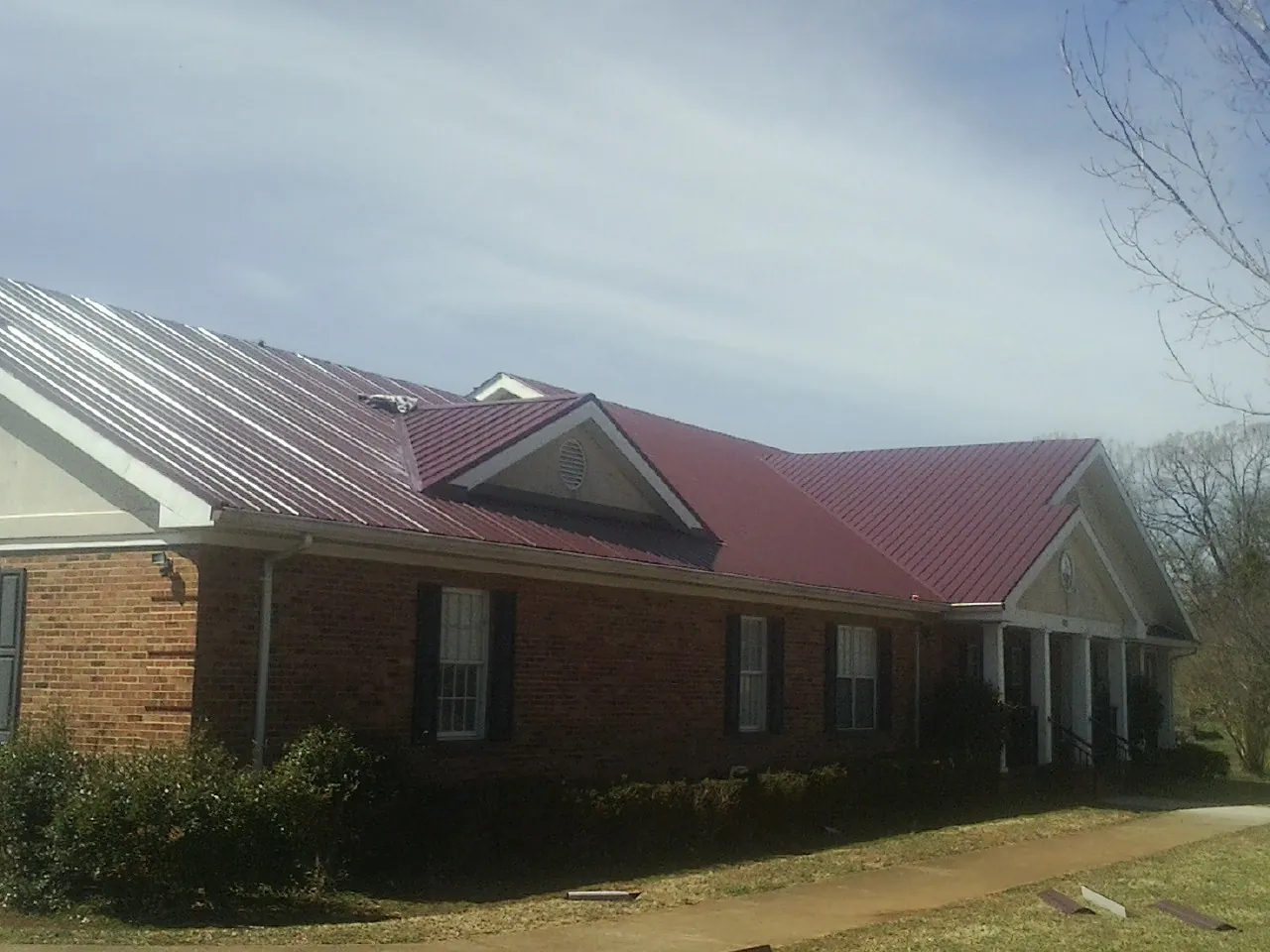 Red metal roof with gabled entries on a long brick building, from a Hail Damage Roof Repair job in Fayetteville