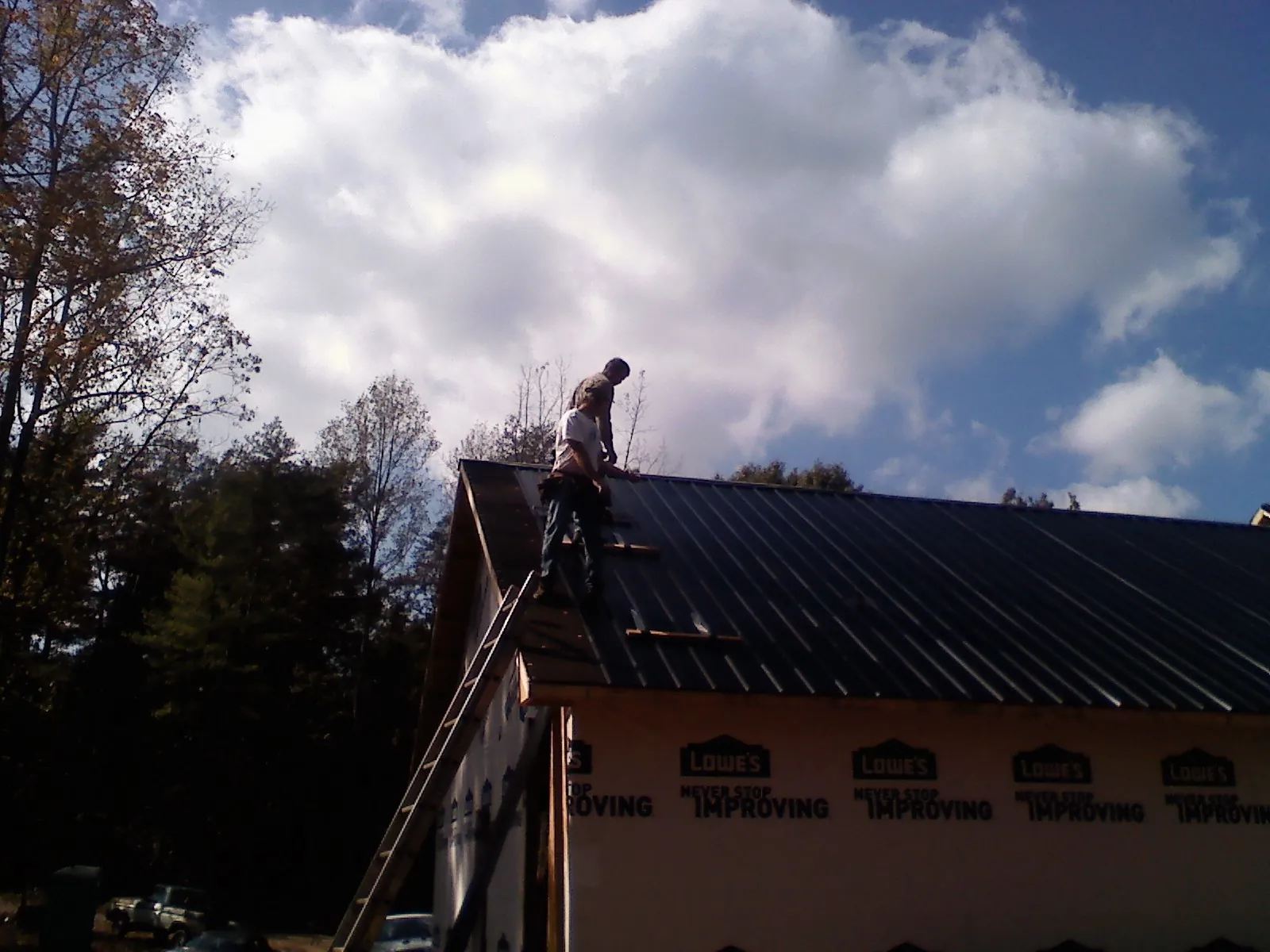 Roofer fastening dark metal panels high against a cloudy sky, from a Roof Inspection job in Fayetteville